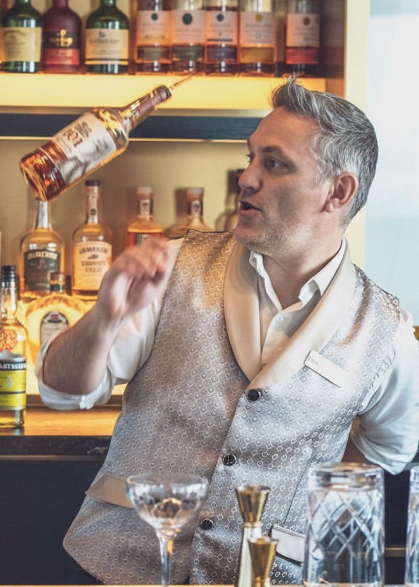 Bartender pouring a drink into a glass with a well-stocked bar in the background of rooftop lounge